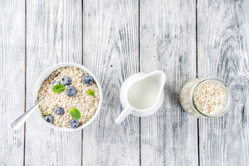 Healthy cereal and milk breakfast concept, dry oats in small bowl, with milk and fresh blueberry, white  wooden concrete background copy space