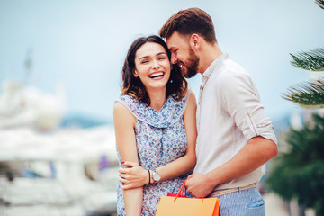 Happy young couple with shopping bags walking by the harbor of a touristic sea resort with boats on background