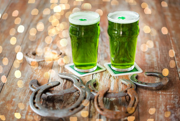 st patricks day, holidays and celebration concept - close up of glasses of green draft beer with shamrock and horseshoe