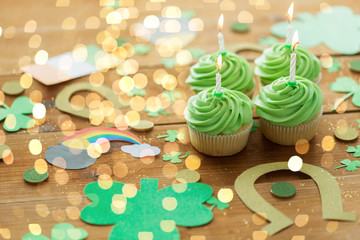 st patricks day, holidays and celebration concept - green cupcakes with candles and other party props on wooden table