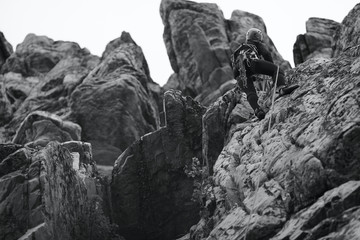 A girl climber climbs the mountains in a complex rocky terrain. Black and white.