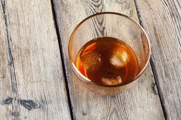 Glass of whiskey on ice with bottle on wood bar