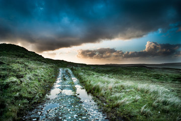 Country road in Ireland at sunset with moody clouds reflecting off of puddles in the road