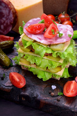Multi layered club sandwich with rye bread, lettuce salad, sausage, cheese, salted cucumbers and tomatoes