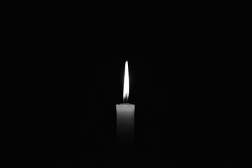Candle burning in the black background. Black and white photo. Located on the center of the shot.