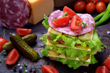 Multi layered club sandwich with rye bread, lettuce salad, sausage, cheese, salted cucumbers and tomatoes