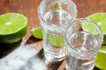 Tequila silver shots with lime slices and salt on wooden board