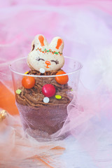 Chocolate mousse in transparent plastic cup, decorated with bunny shaped cookie 
