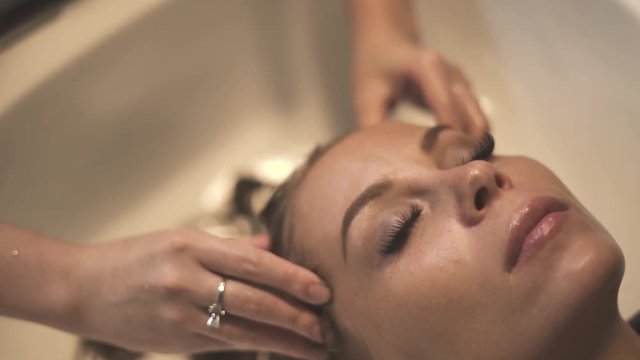 Beautiful woman receiving head massage while washing hair in spa salon Close up hairdresser doing head massage with treatment mask for hair in hairdressing salon. Professional care in beauty studio.