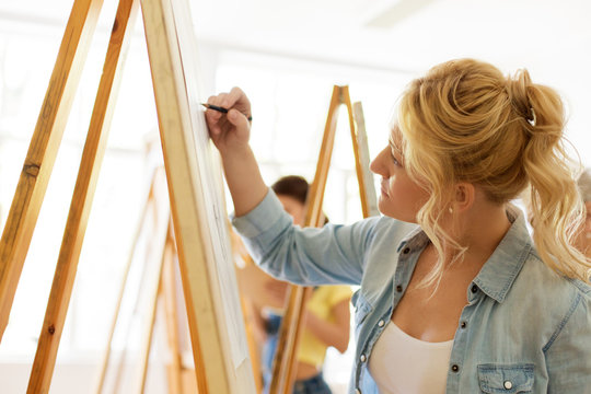 art school, creativity and people concept - woman with easel drawing at studio