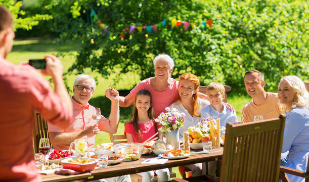 leisure, holidays and people concept - happy family having festive dinner or summer garden party and photographing by smartphone