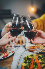 Vertical image of hands making cheers with glasses of red wine during holiday dinner at restaurant, happy friends having birthday party enjoying tasty food, Celebration Friendship Dinner Concept