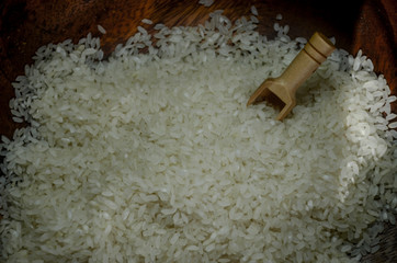 Raw white rice in wood bowl with wood spoon.