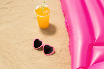 vacation and summer holidays concept - pink sunglasses, orange juice and swimming mattress on beach sand