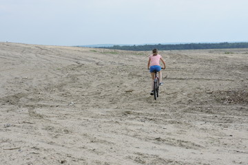 A woman riding a bike on a desert - obrazy, fototapety, plakaty