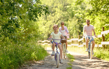 family, leisure and people concept - happy mother, father and little daughter riding bicycles in...