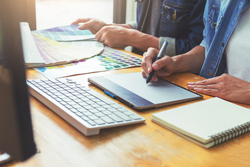 Graphic design with color swatches and tablet on a desk. Graphic designer drawing something on tablet at the office with work tools and accessories.