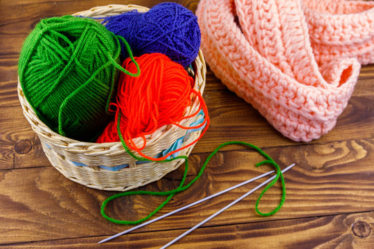 Wicker basket with colorful knitting yarns, knitting needles and knitted scarf on wooden table