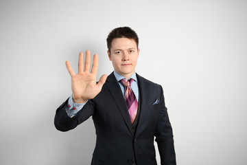 Young businessman in suit on gray background holds his hand in front of him, stop sign.