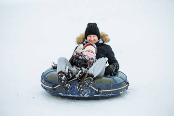 young father slides down from the snow hill on a tube with his little daughter