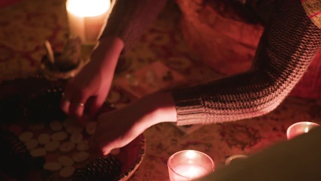 Young woman organizes small runestones in candelit room in meditation ritual