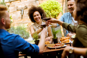 Cheerful young people have lunch in the courtyard and toasting with red wine