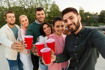 leisure and people concept - happy friends with drinks taking selfie at rooftop party in summer
