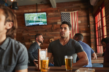 Male Friends Drinking Beer And Watching Game On Screen In Sports Bar