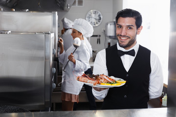 Waiter with dish of seafood in kitchen on restaurant