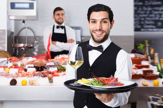 Waiter holding tray with seafood dishes at fish restaurant against backdrop of icy showcase