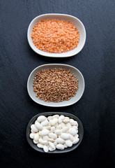 Collection of different groats isolated on black background. Top view of chickpeas, buckwheat, beans in bowls.