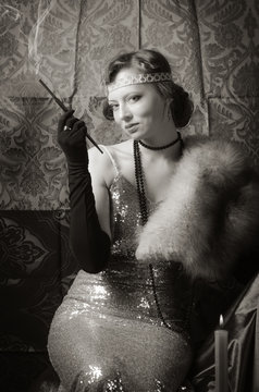 Girl in an evening dress with a cigarette mouthpiece. Studio portrait in retro style, toned in sepia