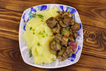 Mashed potatoes with stewed chicken liver with apple and onion on wooden table