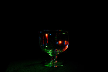 Empty glass in colorful lights on black background