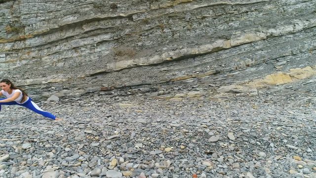 Woman is doing squats the bodyflex during breathing exercises on the rock background. Aerial beautiful footage view.