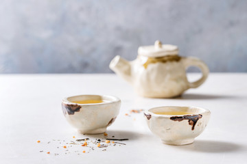 Hot green tea in two traditional chinese clay ceramic cup and teapot standing on white marble table.