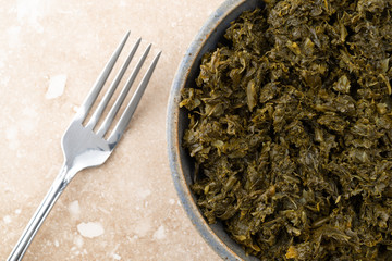 Bowl of chopped kale on a marble table with a fork to the side.