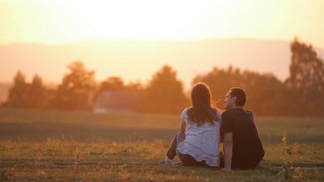 Couple of romantic lovers sitting on summer field embraced of sunset warm light