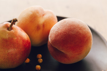 still life - juicy velvety peaches, large ripe pear, and sea buckthorn berries in a ceramic plate on a wooden background