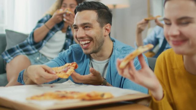 At Home Diverse Group Friends Watching TV Together, They Share Gigantic Pizza, Eating Tasty Pie Pieces. Guys and Girls Watching Comedy Sitcom or a Movie, Laughing and Having Fun Together.