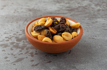 Small bowl filled with peanuts and raisins on a gray background illuminated with natural lighting.