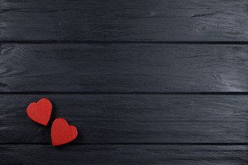 The romantic background with two red wooden hearts on a black wooden background.
