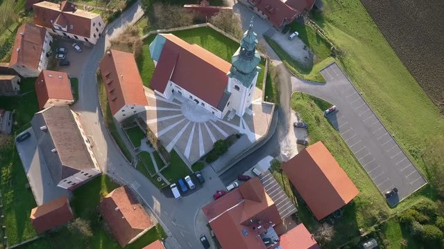 Aerial: Flying arround catholic church with high bell tower at top of small hill. Filming small city surroundings on beautiful spring sunny day.