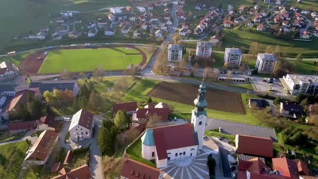 Aerial: Flying arround catholic church with high bell tower at top of small hill. Filming small city surroundings on beautiful spring sunny day.