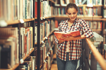 Young female student read and learns by the book shelf at the library.Reading a book.
