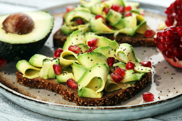 sliced avocado and ripe pomegranates on toast bread with spices and avocado.