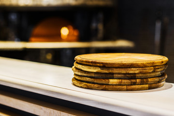 Stack of wooden boards in front of traditional pizza oven