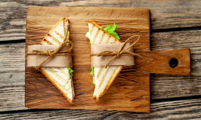 two sandwiches from the store wrapped in paper on a cutting board, wooden background