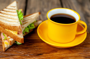 two delicious sandwiches with ham, cheese, lettuce and a cup of coffee on a wooden background