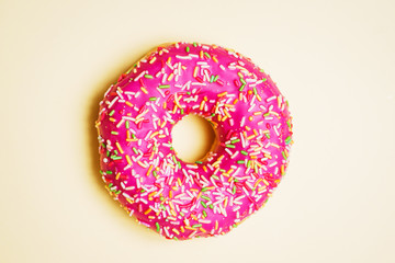 Bright donut in a pink glaze with a multi-colored rainbow sprinkle on a yellow background. 